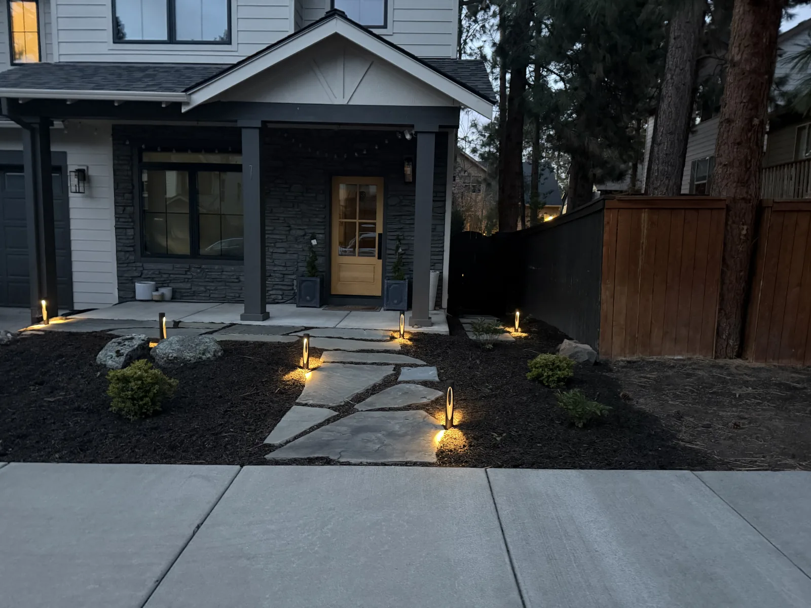 Low-voltage path lights illuminating a flagstone walkway and entry porch at dusk on a modern Bend, Oregon home
