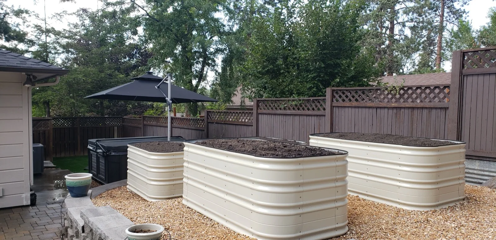 Contemporary raised garden beds on a gravel base with patio umbrella for a functional backyard growing space.